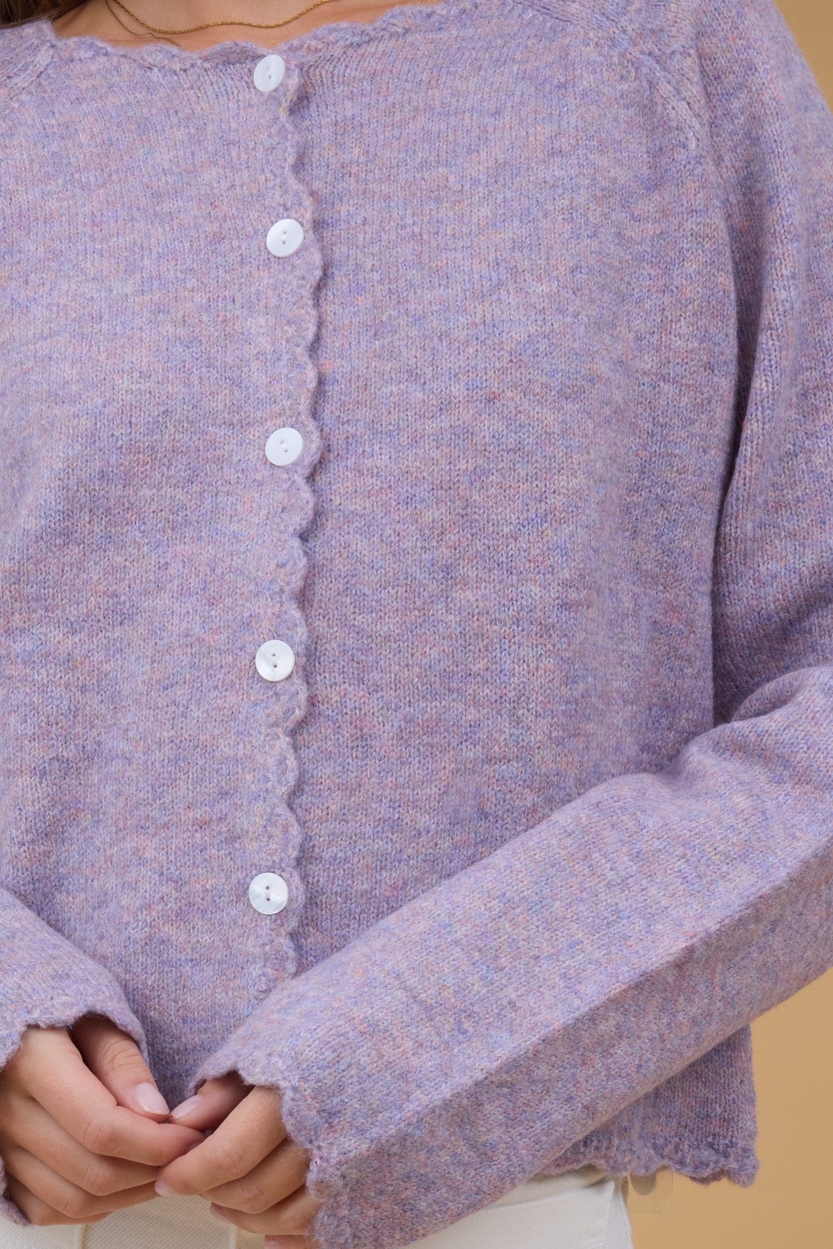 Close up view of a button down cardigan with scallop hems and edges.