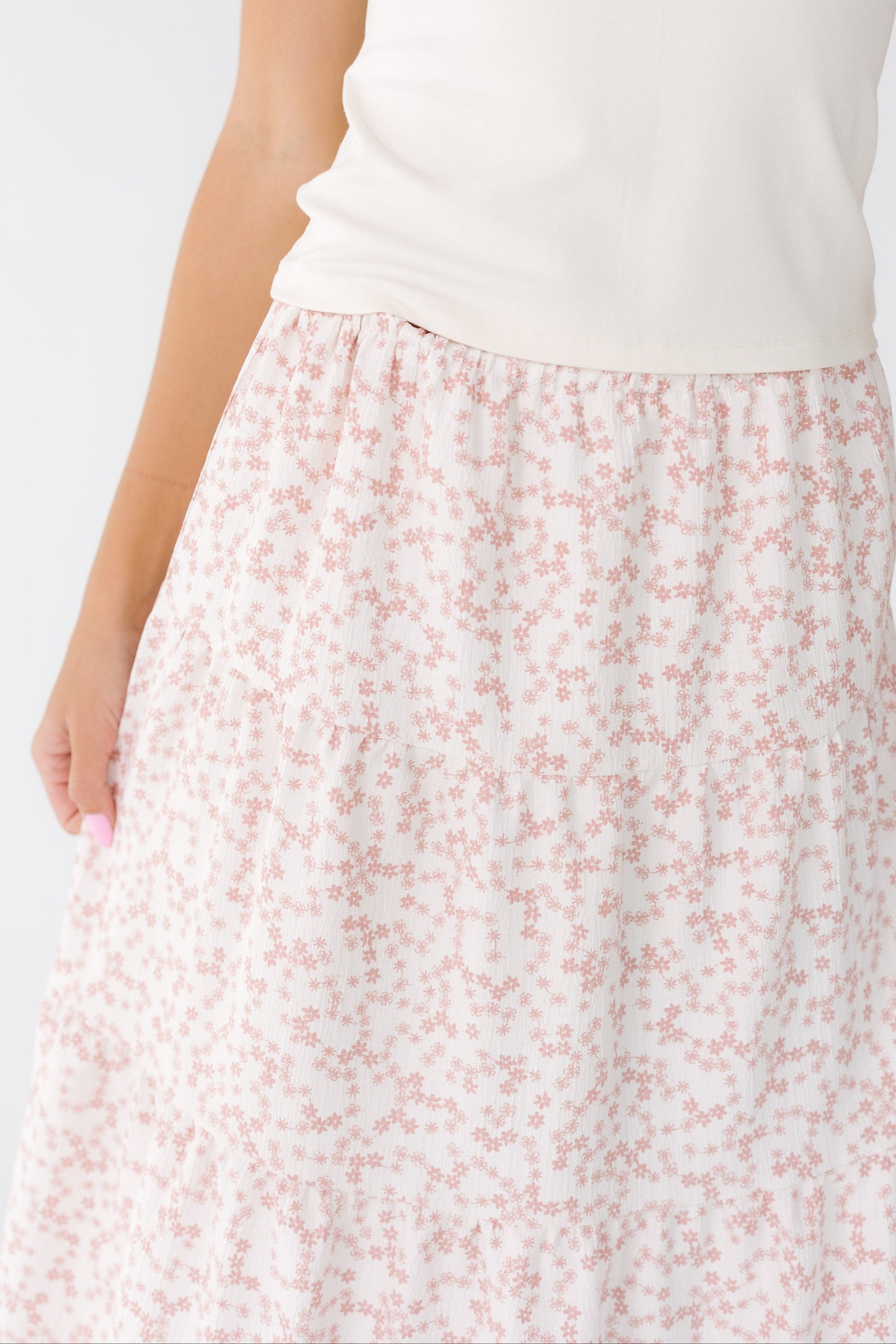 Close view of a young woman wearing a white and pink floral midi skirt with multiple gathered tiers.