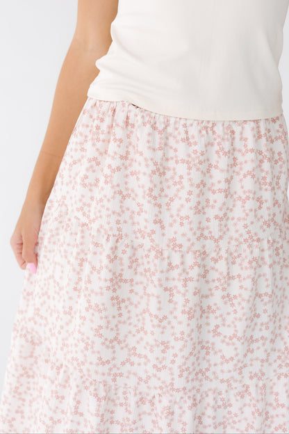 Close view of a young woman wearing a white and pink floral midi skirt with multiple gathered tiers.