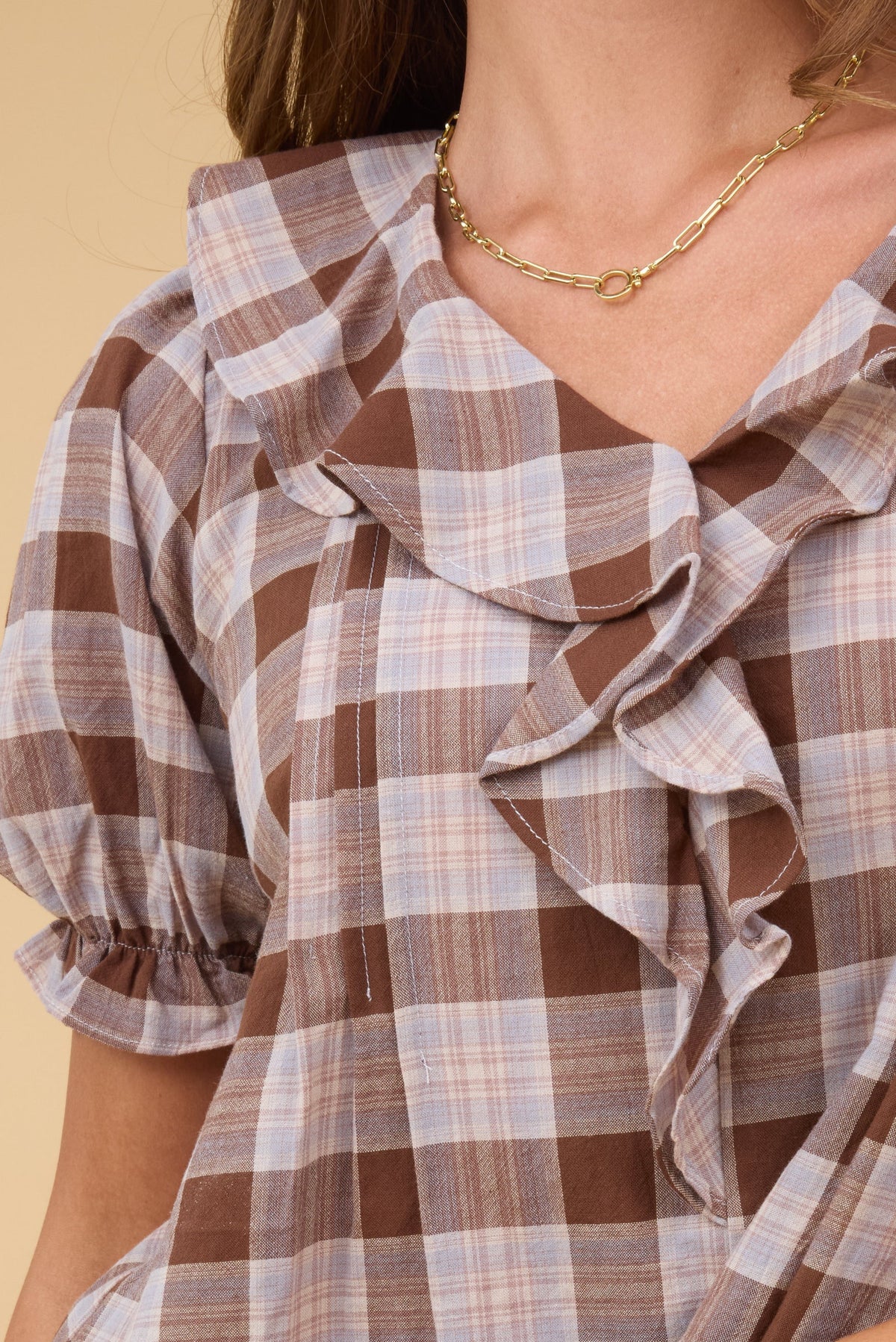 A close up view of a young woman wearing a brown plaid blouse with short sleeves and a ruffle collar.