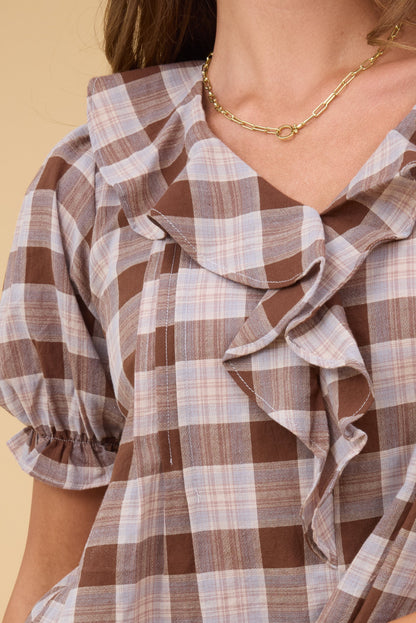 A close up view of a young woman wearing a brown plaid blouse with short sleeves and a ruffle collar.