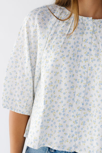 Close view of a young woman wearing a white and blue loose fitting button down top with elbow length sleeves.