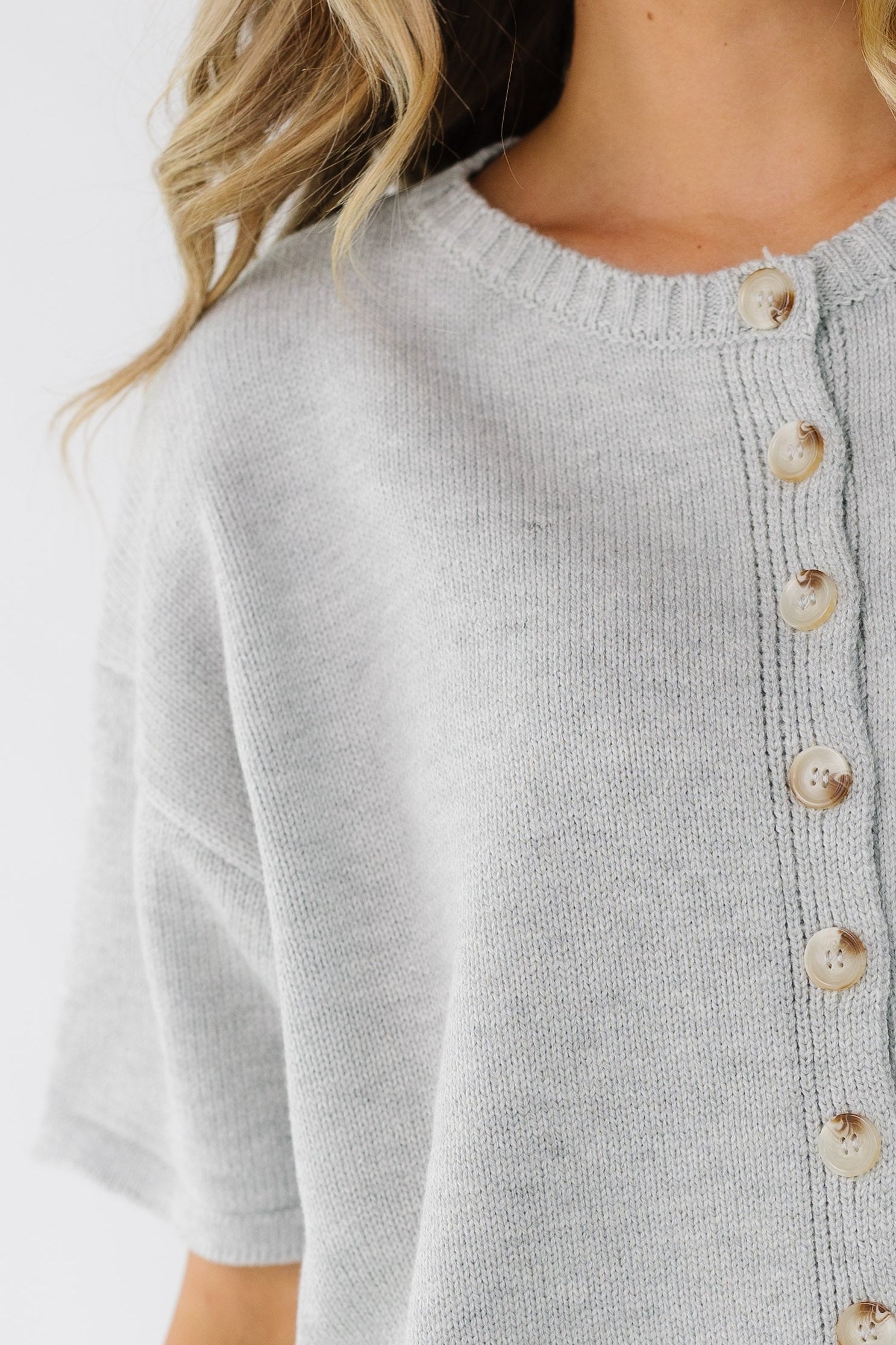 Close view of a woman wearing a grey short sleeve button down cardiagn.