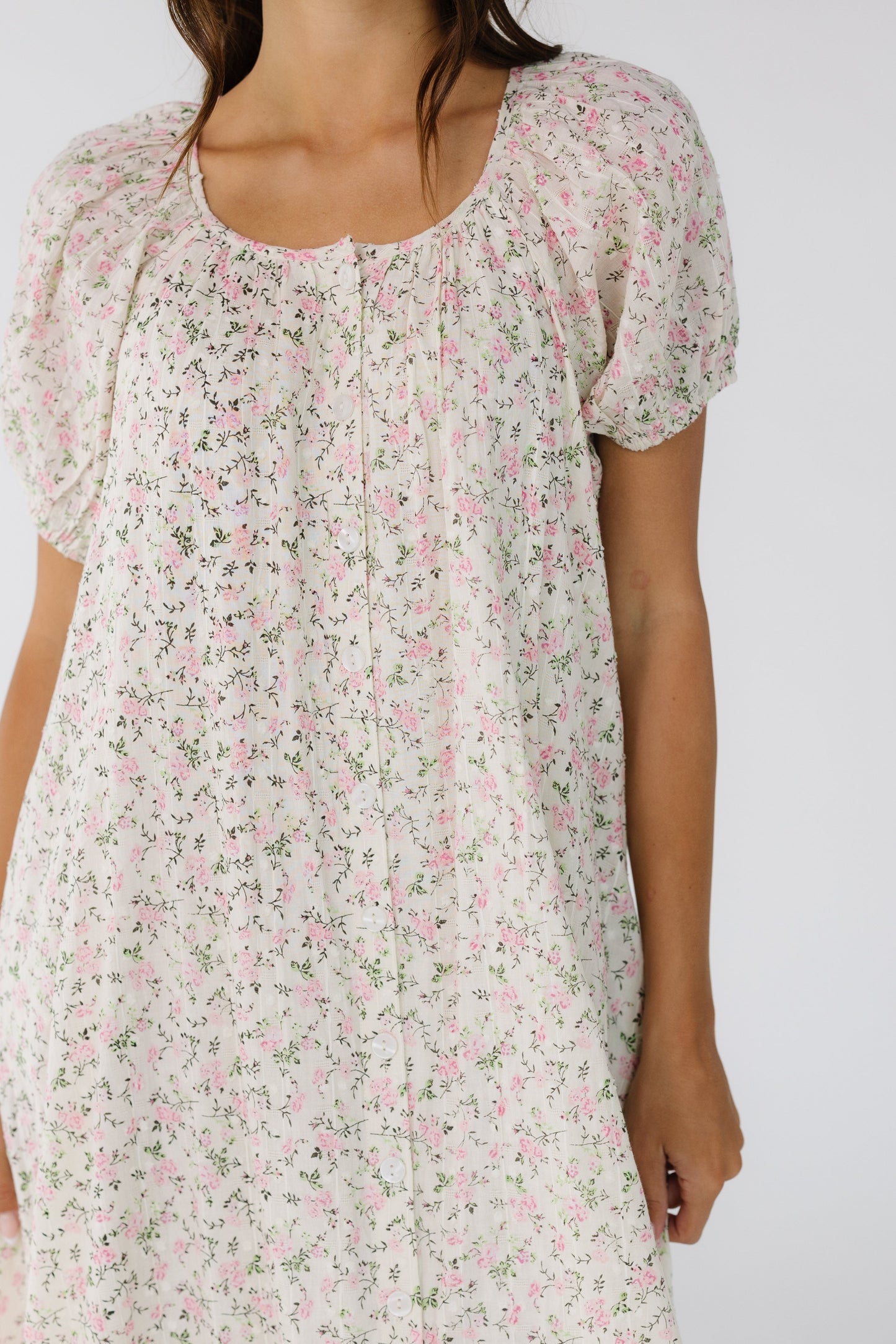 Close view of a woman wearing a  button down dress with a scoop neckline and large puff sleeves. 
