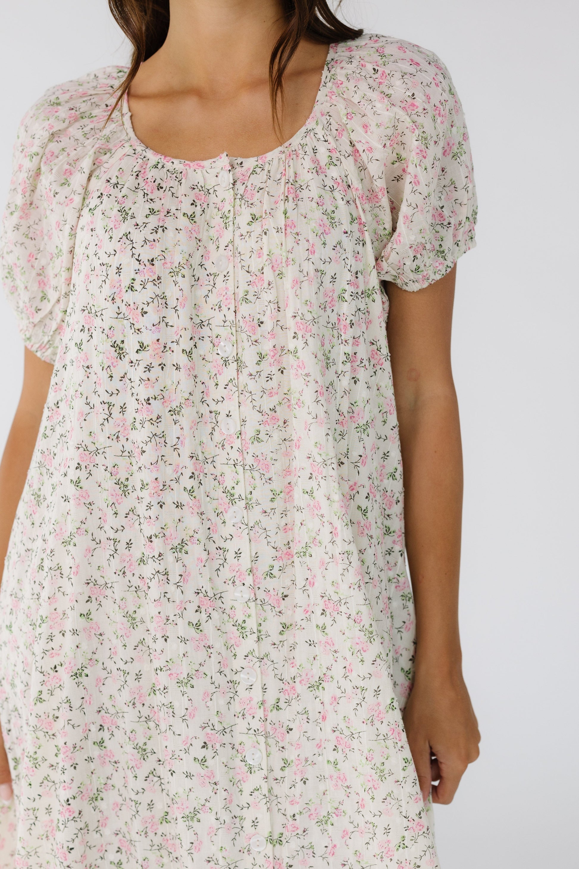 Close view of a woman wearing a  button down dress with a scoop neckline and large puff sleeves. 