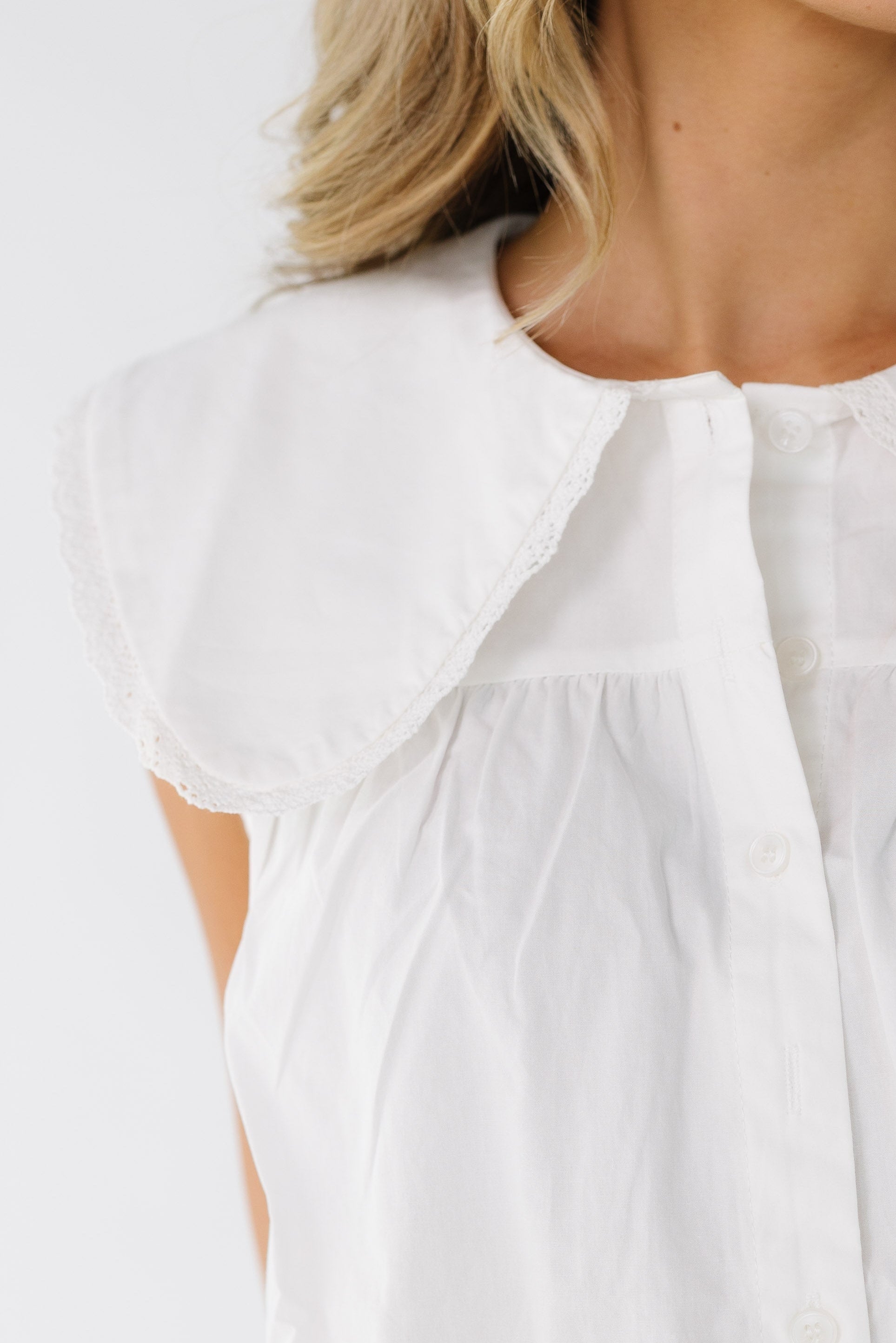 Close view of a woman wearing a white button down top with a lace trimmed wide collar with rounded points.