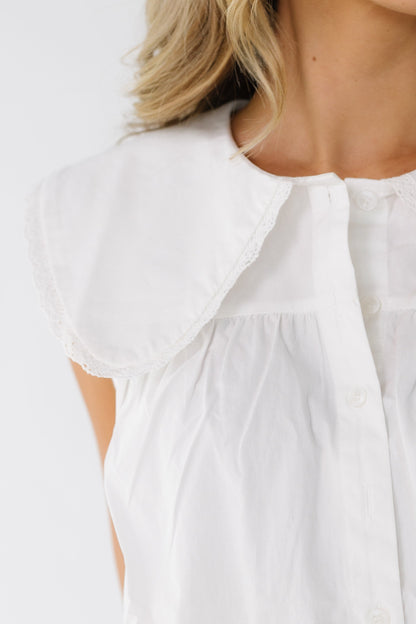 Close view of a woman wearing a white button down top with a lace trimmed wide collar with rounded points.