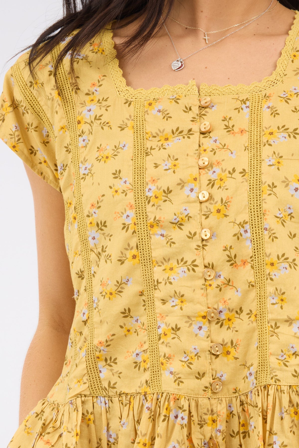 A close view of a woman wearing a yellow floral print blouse iwth lace & ruffles.