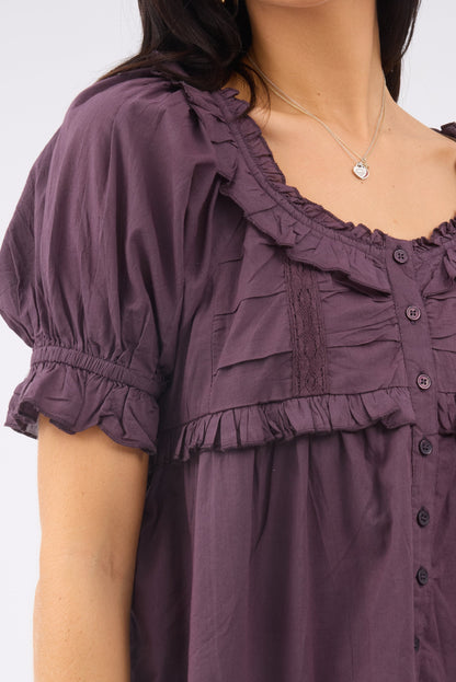 A close up view of a woman wearing purple button down blouse with ruffle  lace details.