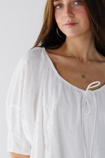 Close view of a woman wearing a white eyelet dress with elbow length sleeves and a drawstring scoop neckline.