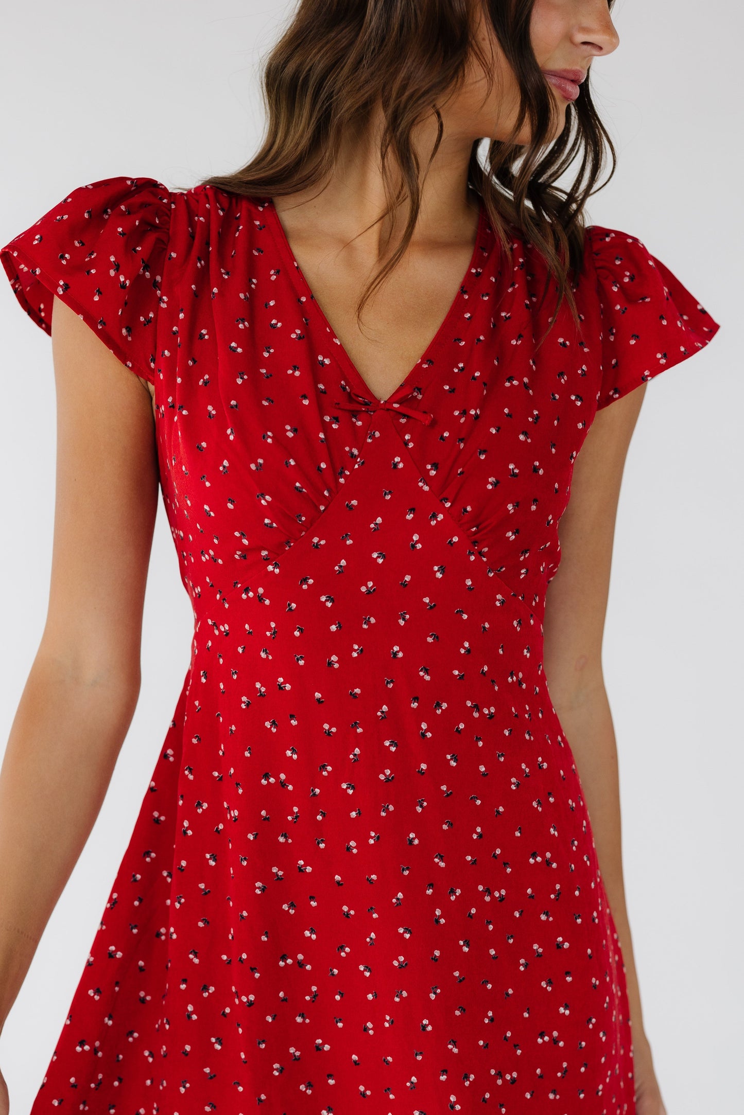 Close view of a woman wearing a red dress with  short flutter sleeves, a V-neckline and a high pointed empire waist.