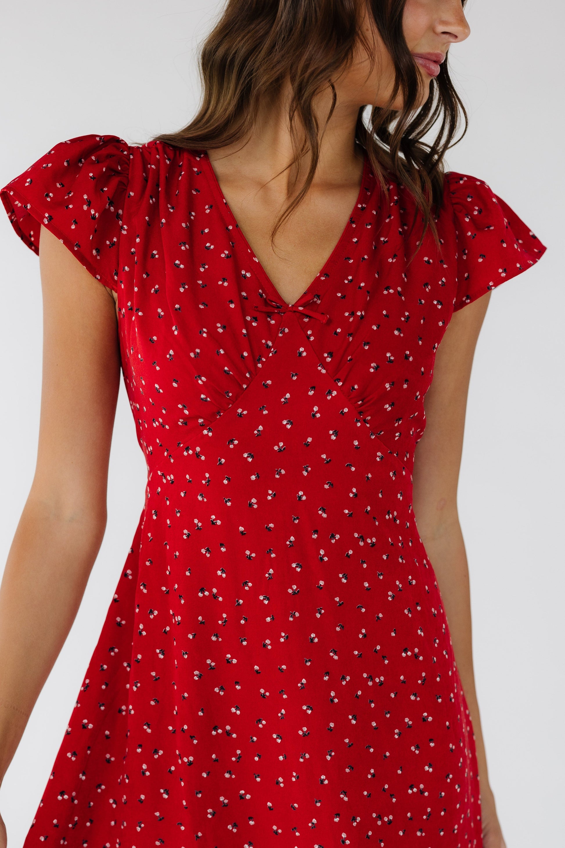 Close view of a woman wearing a red dress with  short flutter sleeves, a V-neckline and a high pointed empire waist.
