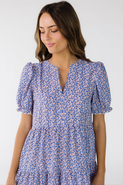 Close view of a young woman wearing a purple floral dress with a V-neckline and short puff sleeves.