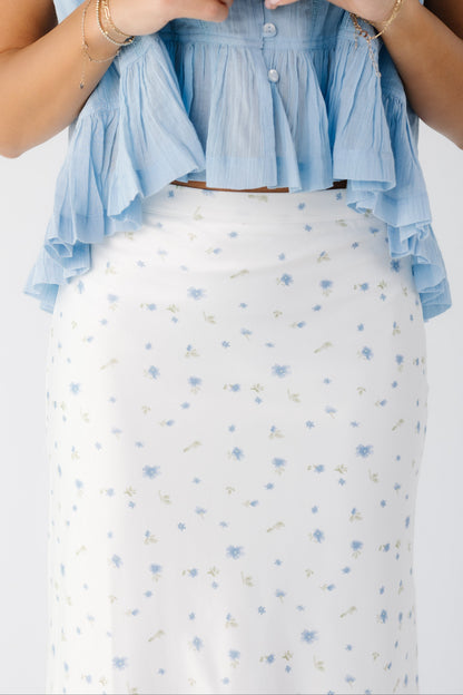 Close up view of a young woman wearing an off white midi skirt with a blue scattered floral print.