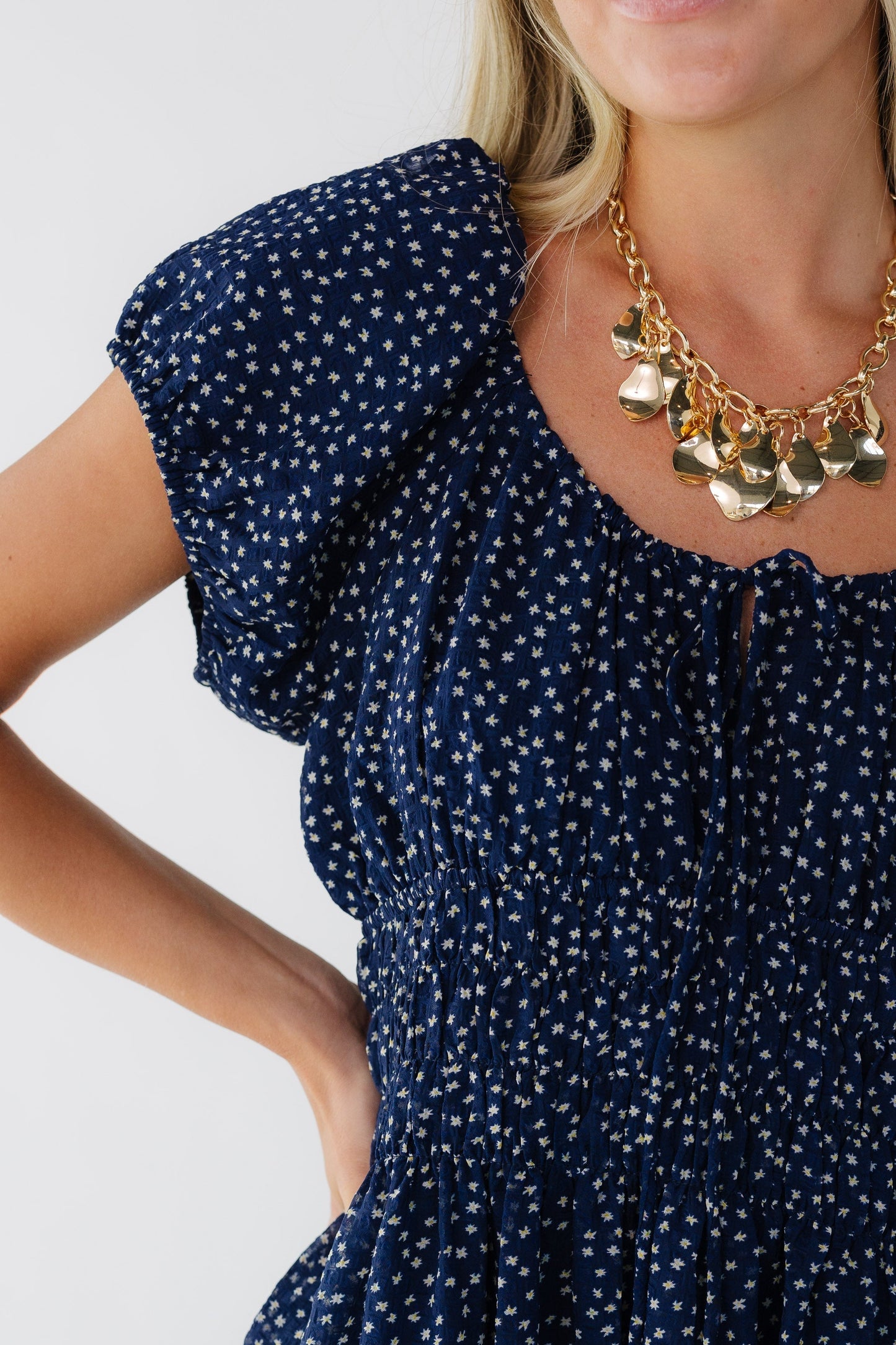 Close view of a woman wearing a navy print dress with a scoop neckline, wide elastic waistband and short puff sleeves.