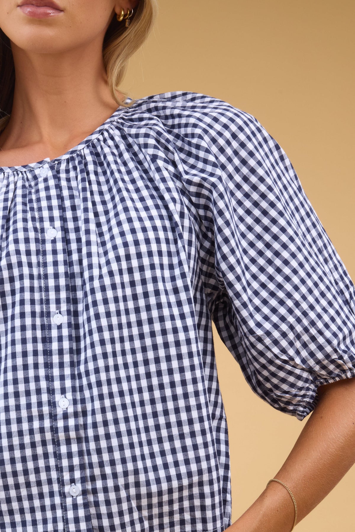 Close view of a woman wearing a navy & white gingham, button down blouse and a round neckline.