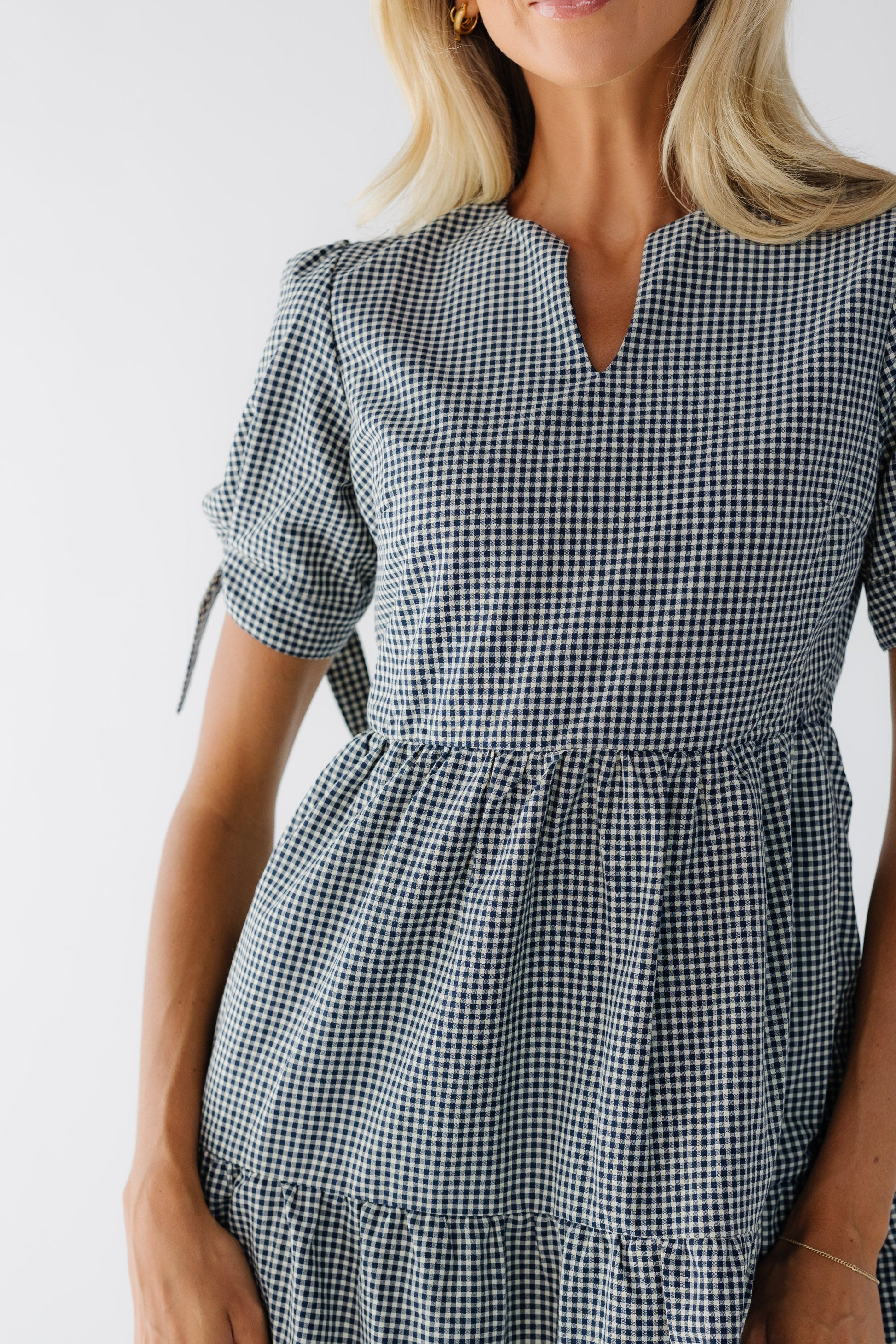 Close view of a woman wearing a navy & white gingham dress with with a closer fitting bodice and short puff sleeves.