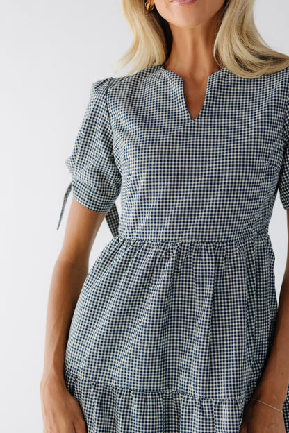 Close view of a woman wearing a navy & white gingham dress with with a closer fitting bodice and short puff sleeves.