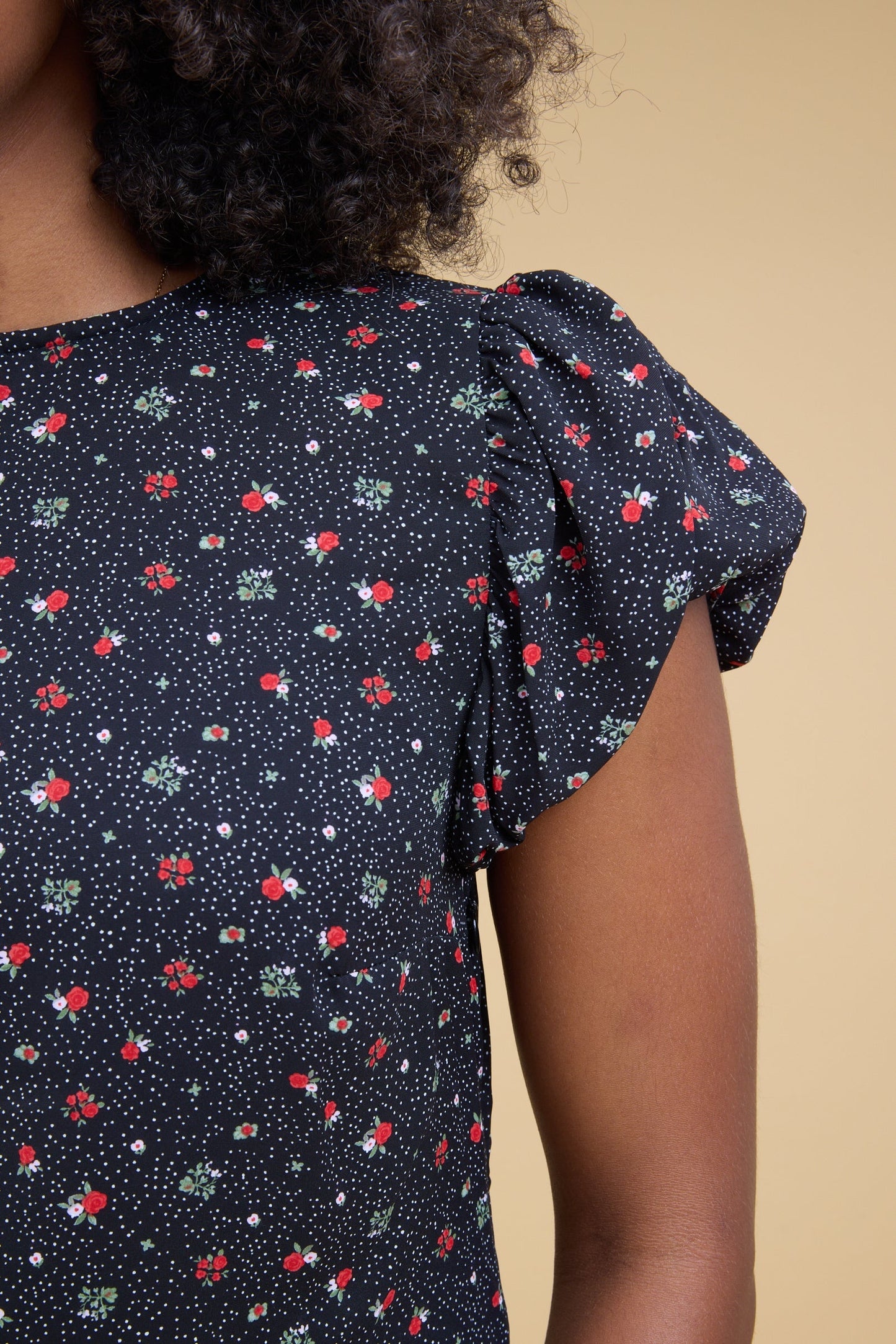 Close view of a young woman wearing a black floral print dress with gathered cap sleeves.