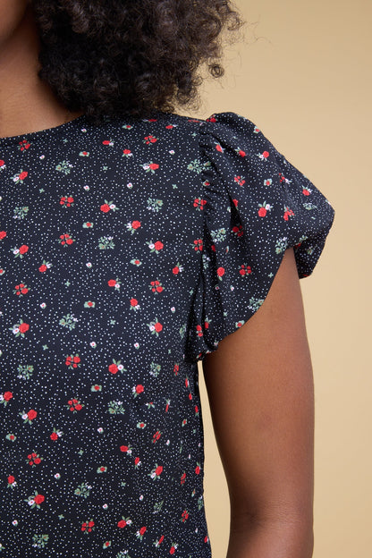Close view of a young woman wearing a black floral print dress with gathered cap sleeves.
