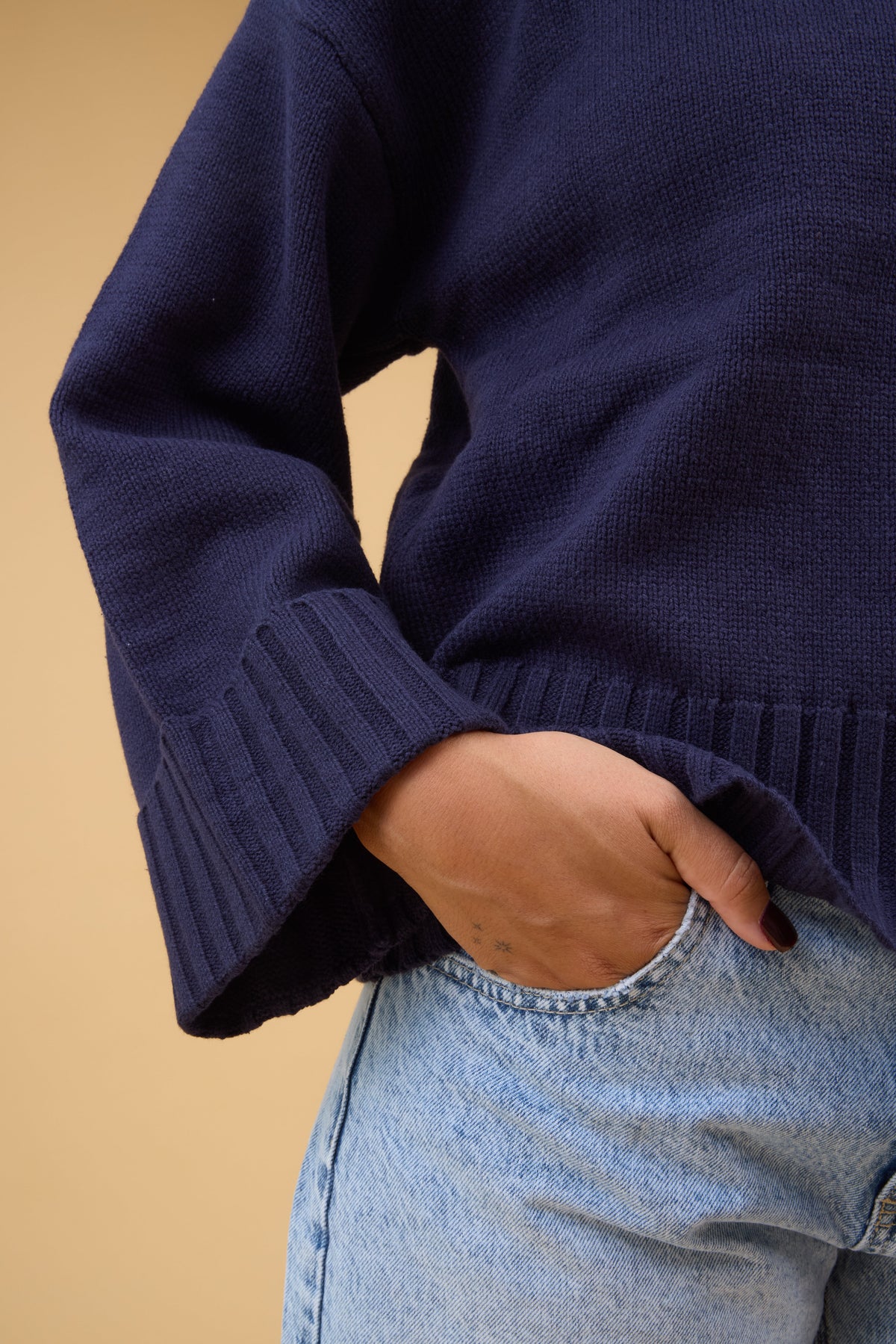 Close view of a woman wearing a a navy sweater with very wide ribbed cuffs and waist.