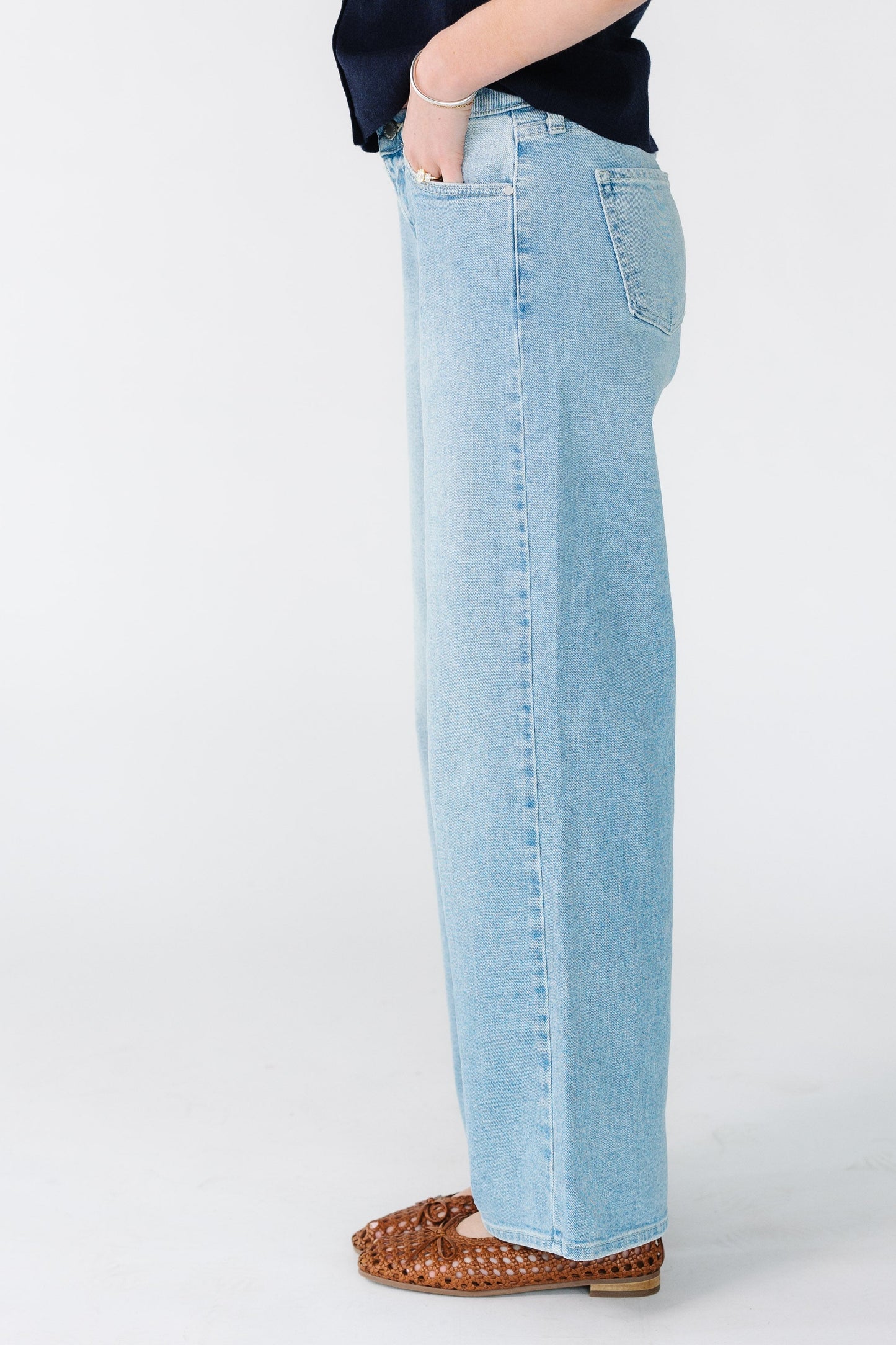 Side view of a woman wearing light denim jeans cut in a wide leg with pockets and sewn hems.