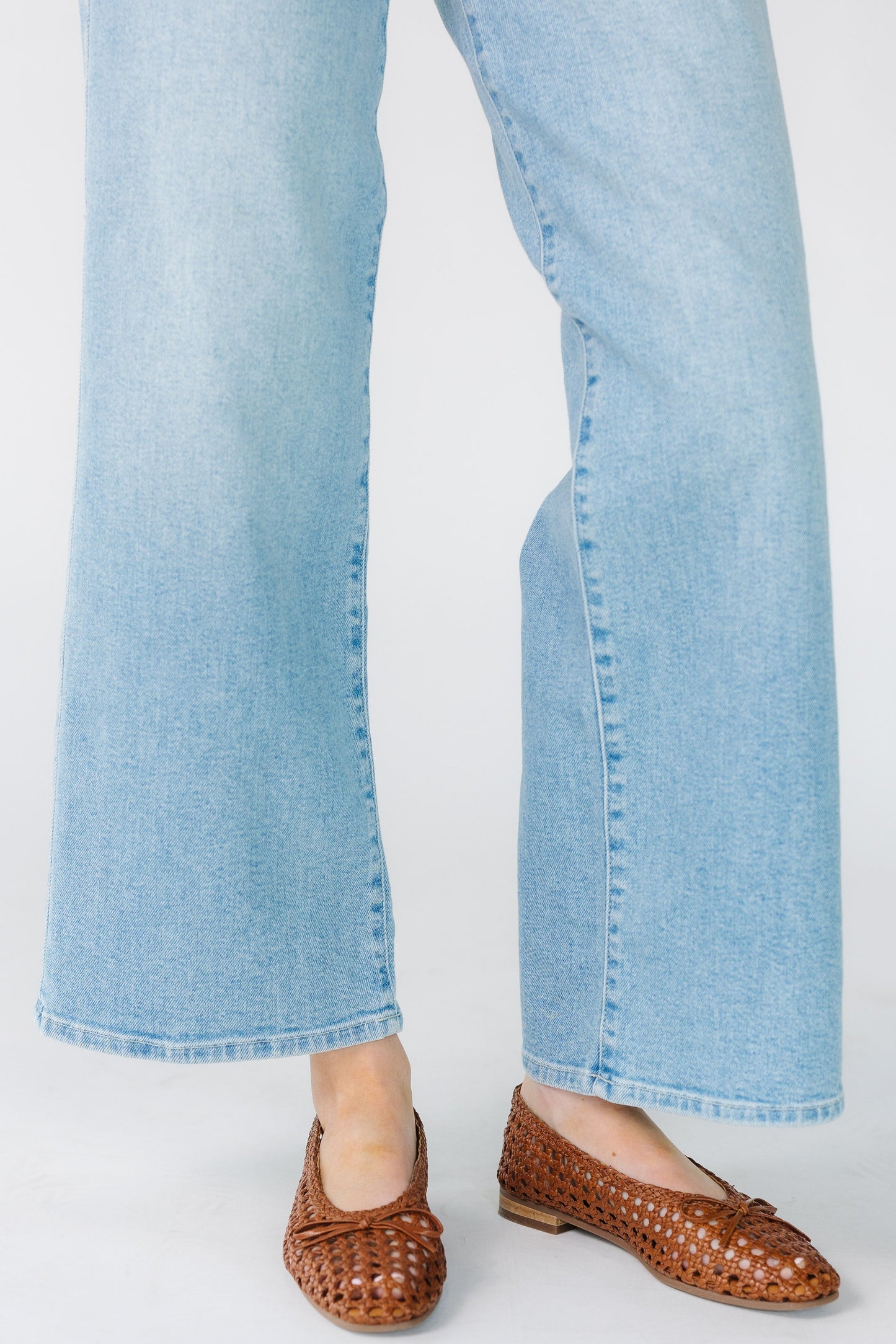 Close view of a woman wearing wide leg jeans in light denim with sewn hems.