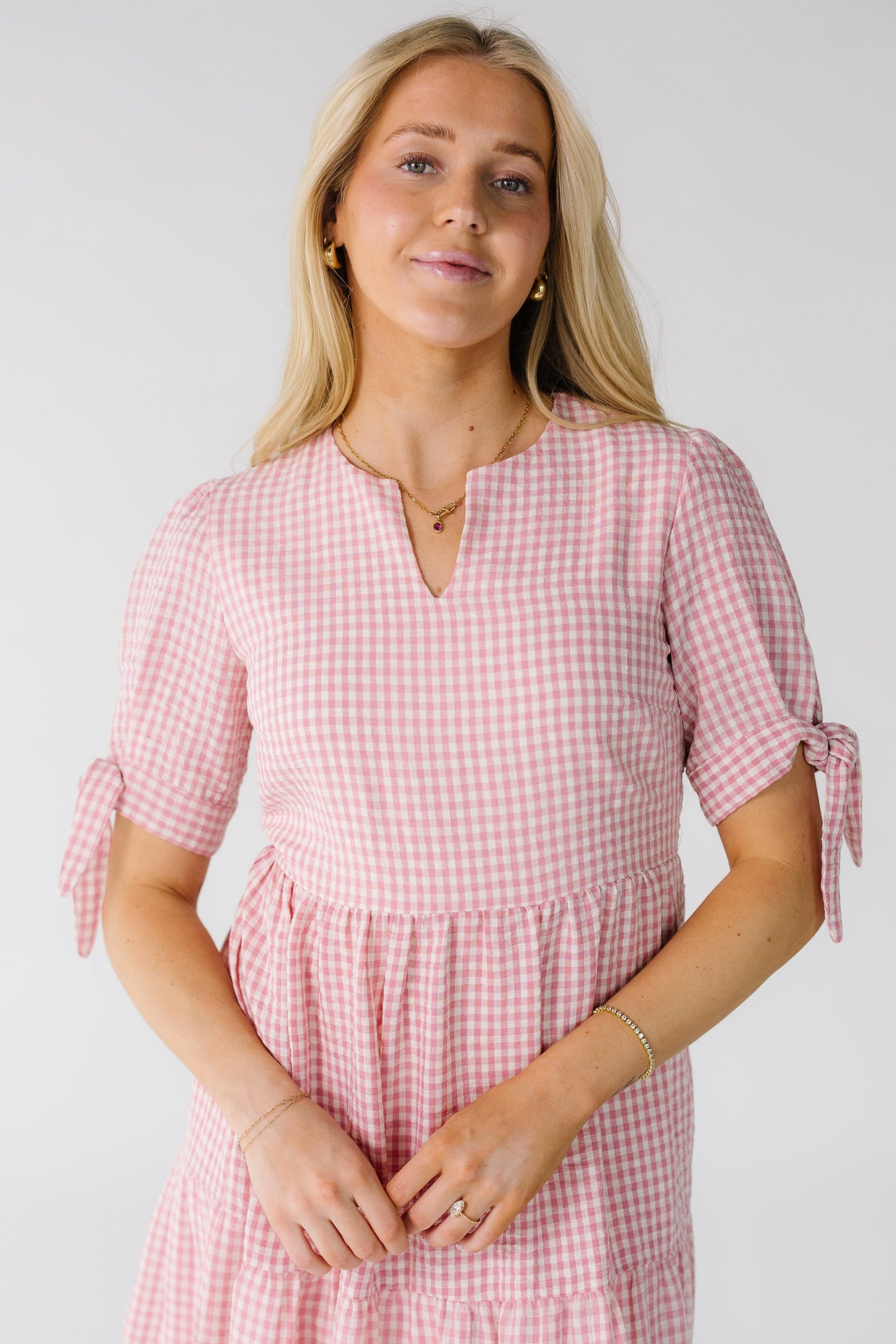 Close view of a woman wearing a pink and white gingham dress with a V-neckline and short sleeves with ties.