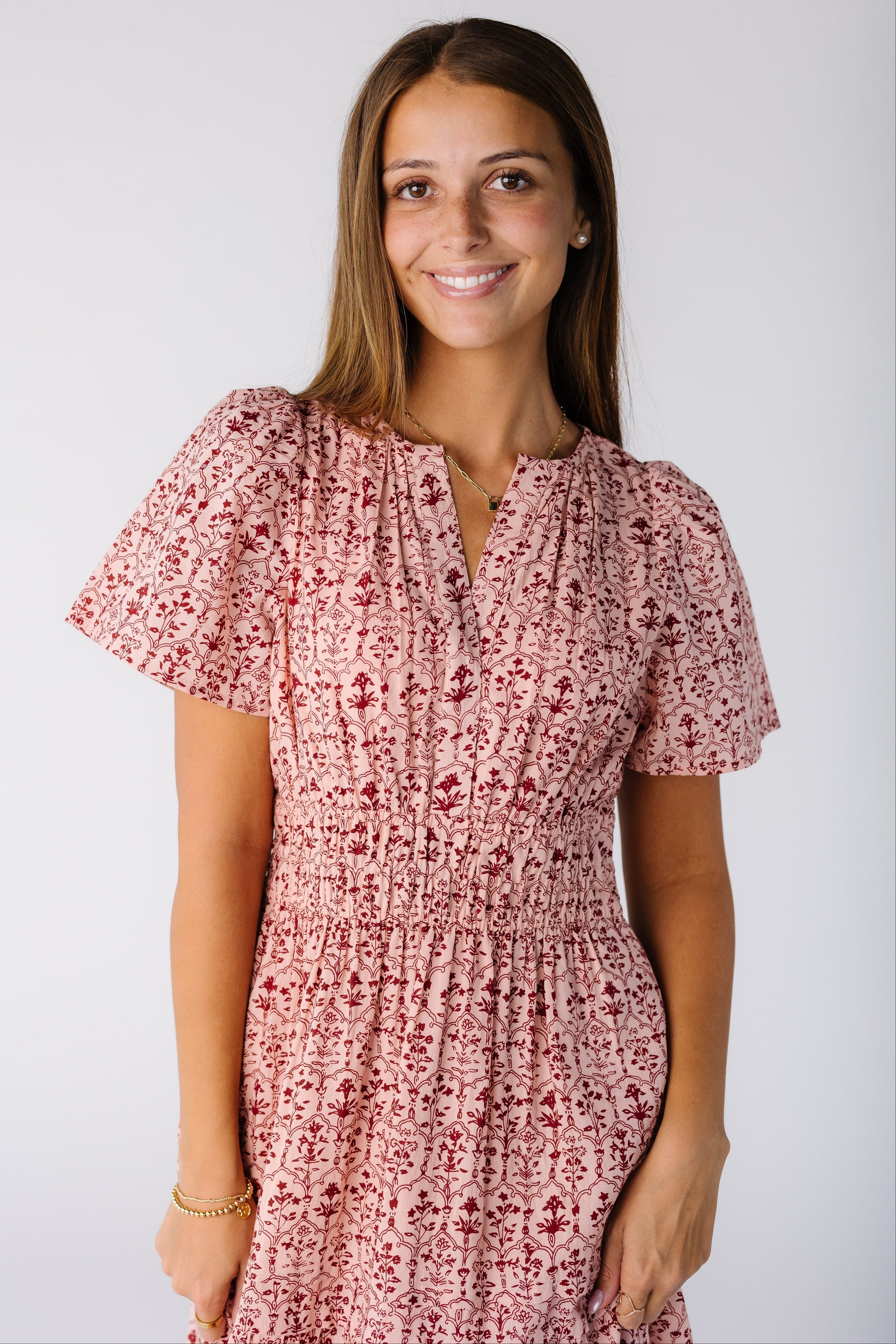Close view of a woman wearing a pink print dress with a V-neckline and short sleeves with a wide elastic waistband