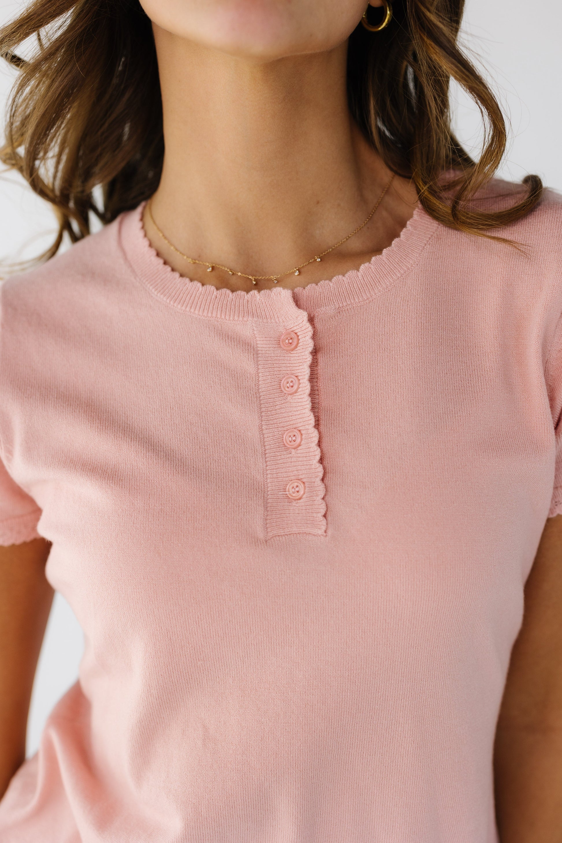 Close view of a young woman wearing a pink kinit top with scallop hems and a short button placket.