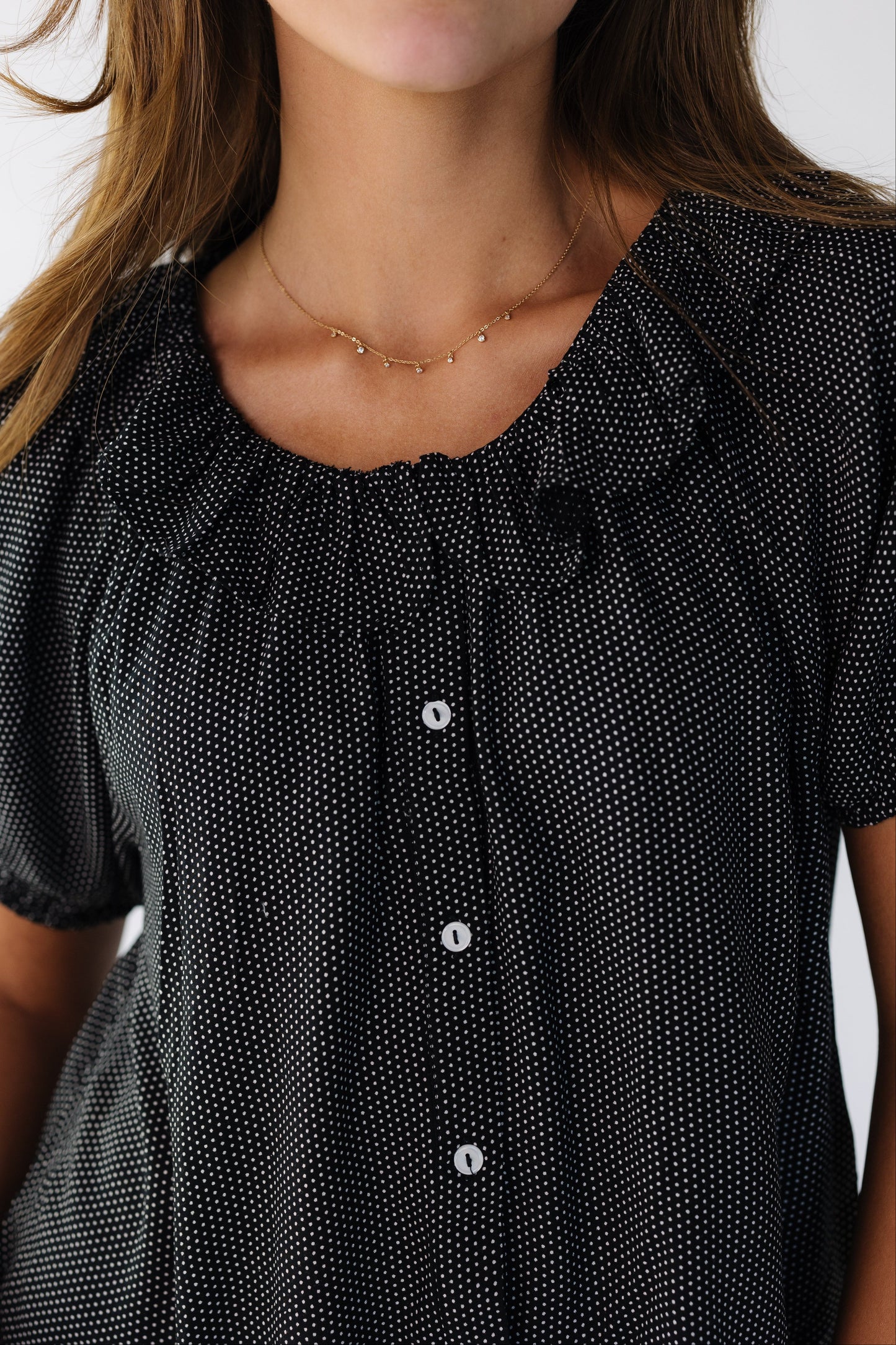 Close view of a young woman wearing a black and white polka dot  button down top with a ruffle, round collar.