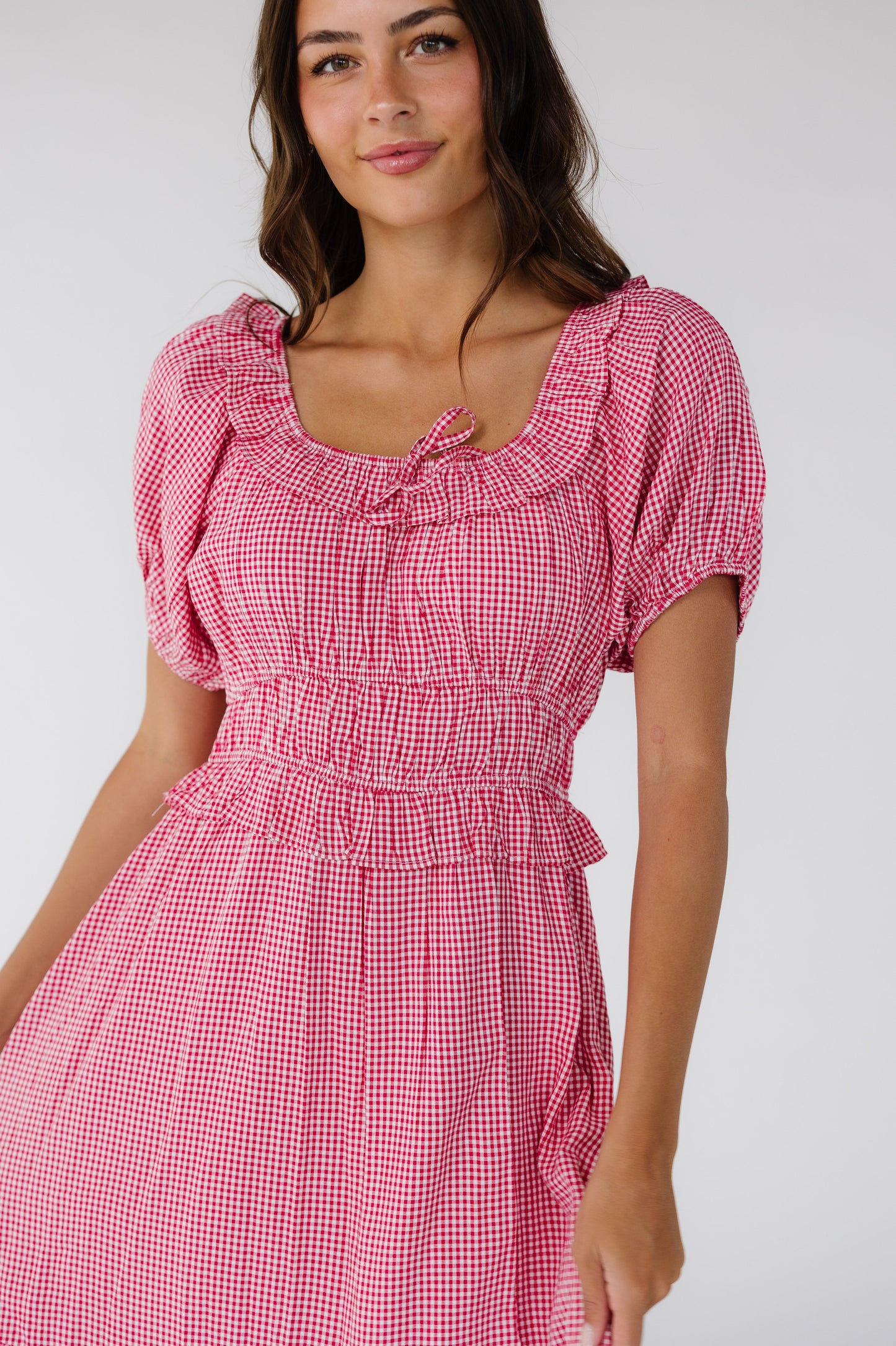 Close view of a woman wearing a red gingham dress with a scoop neckline, short puff sleeves and a wide waistband and a full skirt.
