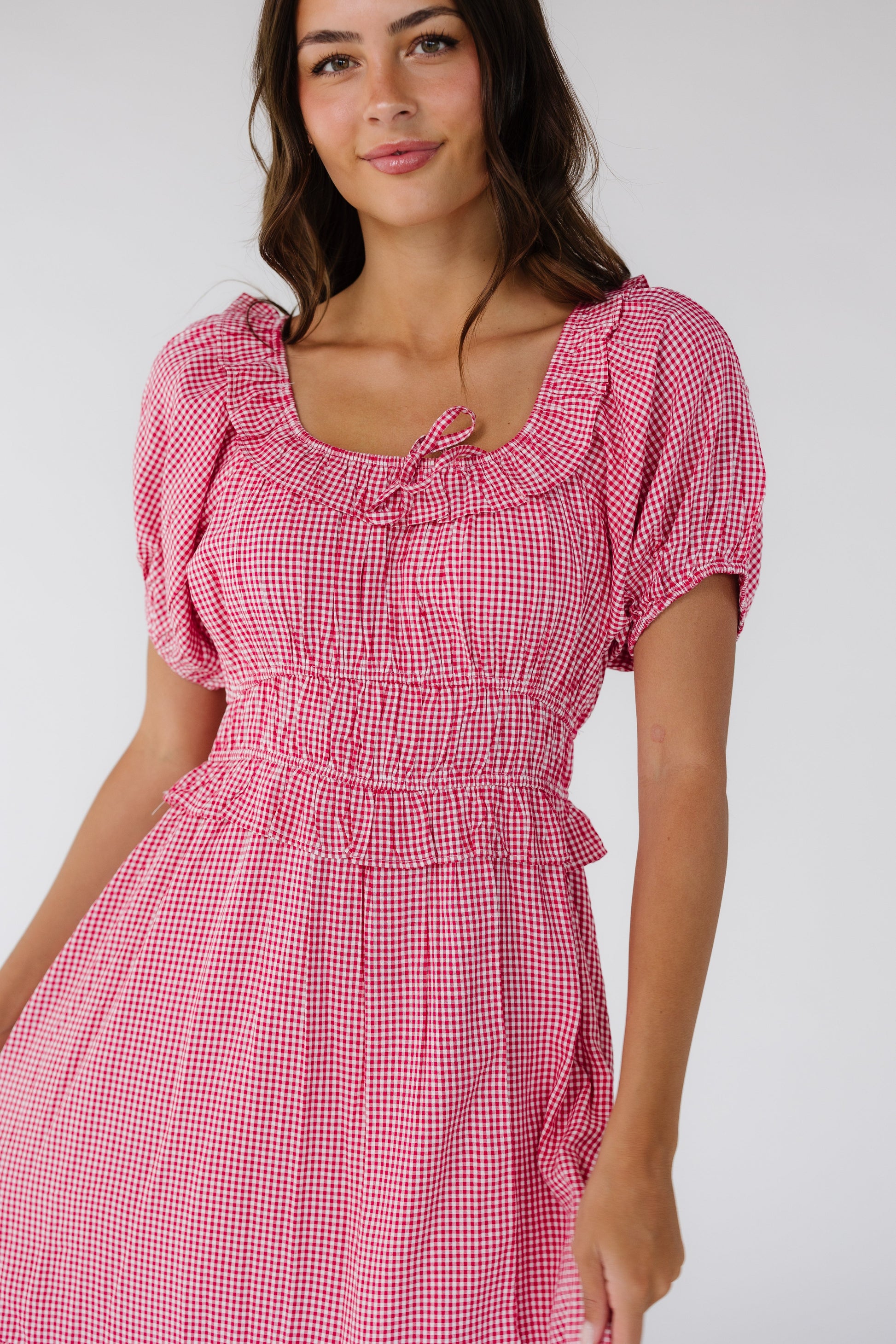 Close view of a woman wearing a red gingham dress with a scoop neckline, short puff sleeves and a wide waistband and a full skirt.
