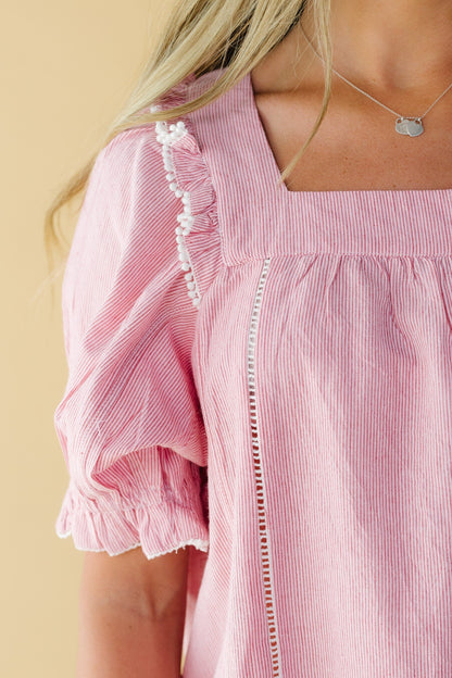 Close view of a young woman wearing a red & white stripe top with a square neckline, short puff sleeves and lace and ruffle details.