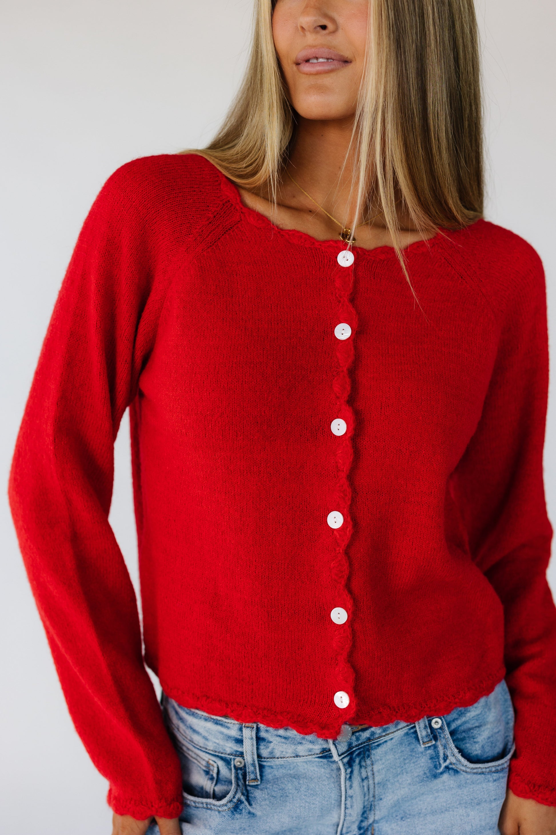 Close view of a woman wearing a red button down cardigan with white buttons and scallop edge neckline, cuffs, hem and button placket.
