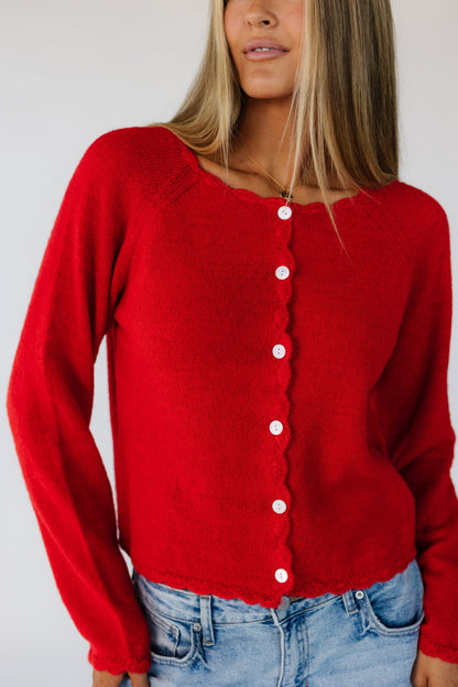 Close view of a woman wearing a red button down cardigan with white buttons and scallop edge neckline, cuffs, hem and button placket.