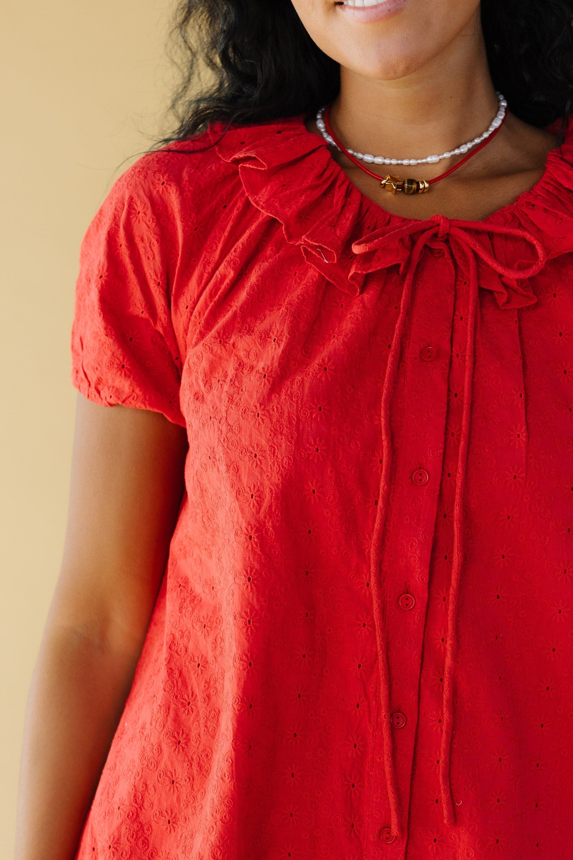 Close view of a woman wearing a red eyelet button down dress with puff sleeves and a round ruffled collar.