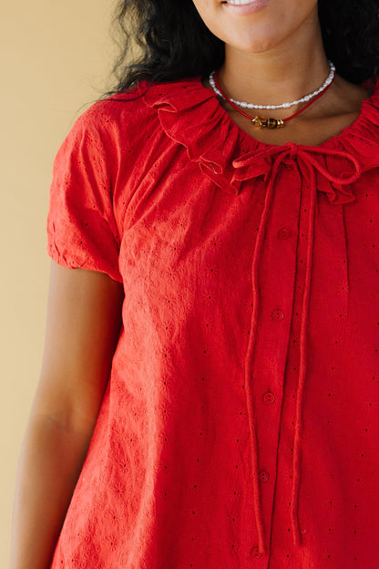 Close view of a woman wearing a red eyelet button down dress with puff sleeves and a round ruffled collar.