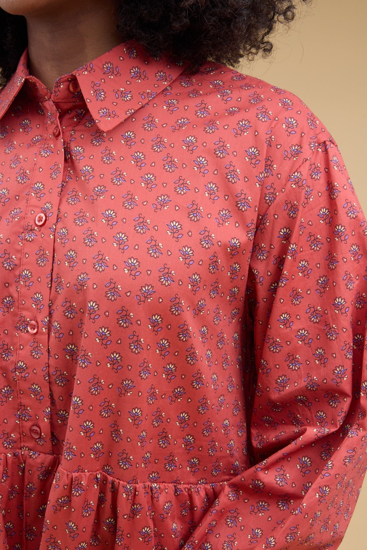 Close view of a young woman wearing a red floral dress with a button down bodice, long sleeves and a pointed collar.