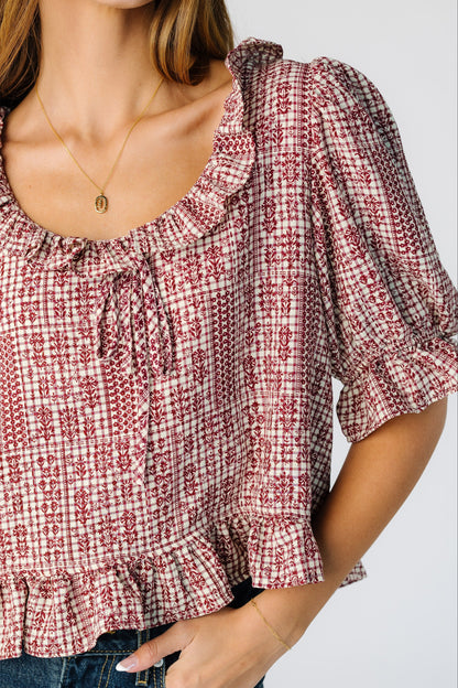 Close view of a woman wearing a red plaid and floral top with ruffles at the neckline, cuffs and waist