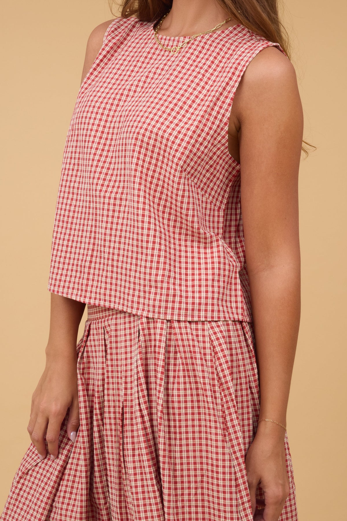 Close view of a woman wearing a red plaid sleeveless top with a full pleated skirt.