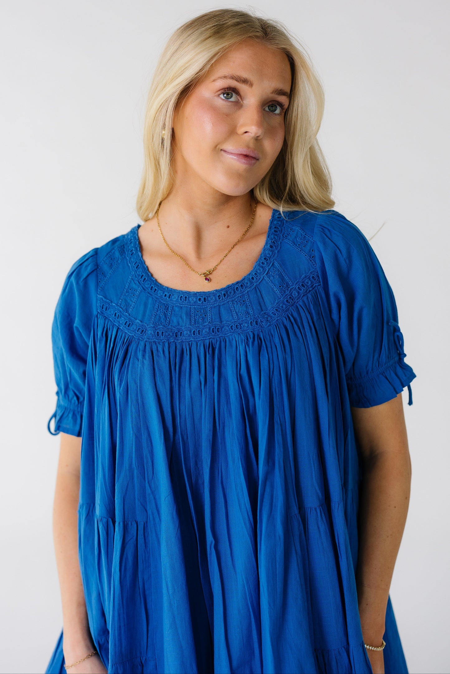 Close view of a woman wearing a bight blue full blue dress with eyelet lace yoke and short puff sleeves.