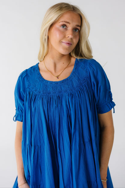 Close view of a woman wearing a bight blue full blue dress with eyelet lace yoke and short puff sleeves.