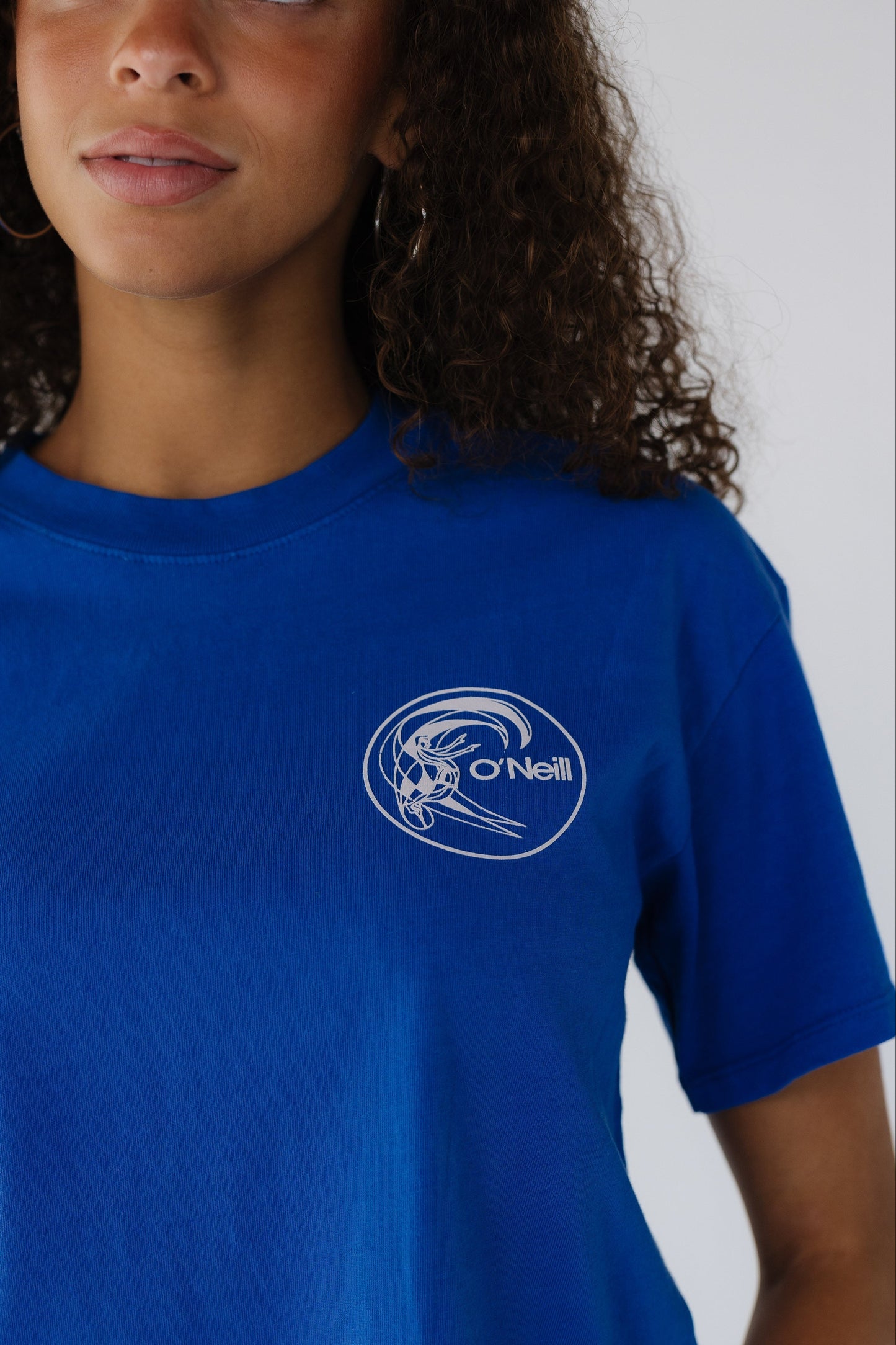 Close view of a woman wearing a blue short sleeve tee with a whtie O'Neill graphic.