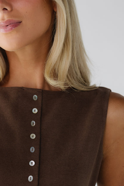 Close view of a woman wearing a sleeveless button down top with a high round neckline in brown.