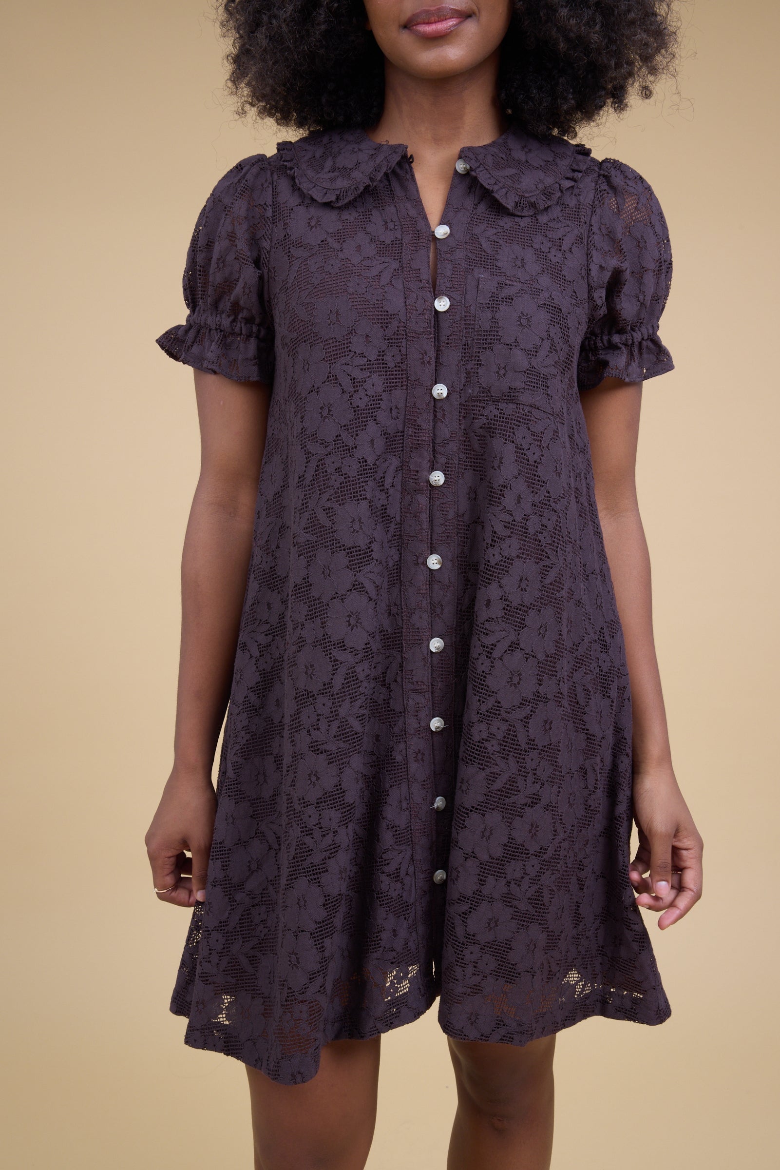 Close view of a woman wearing an all lace short dress in brown with short puff sleeve.