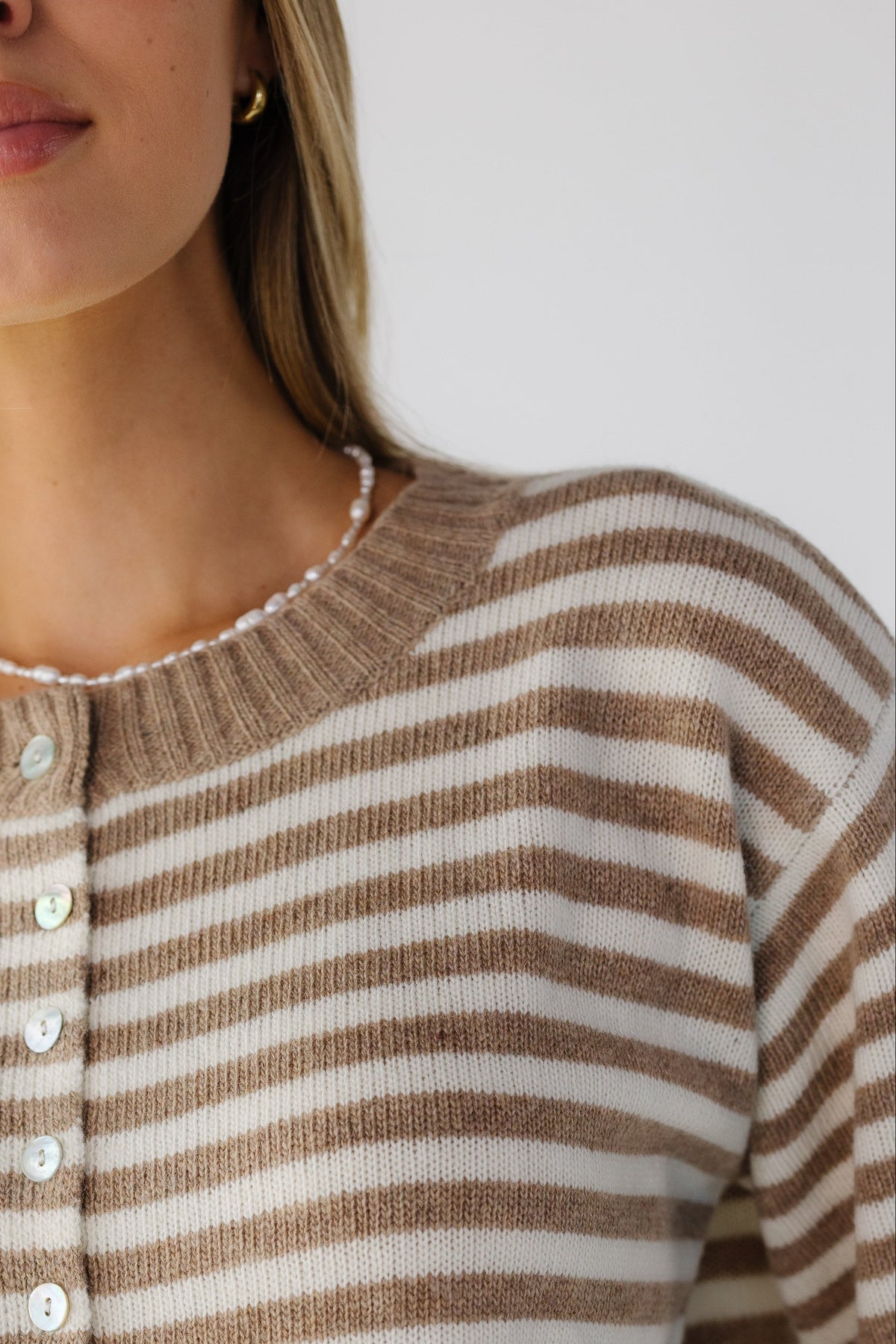 A close up view of a woman wearing a taupe & cream stripe cardigan with a wide ribbed, round neckline.