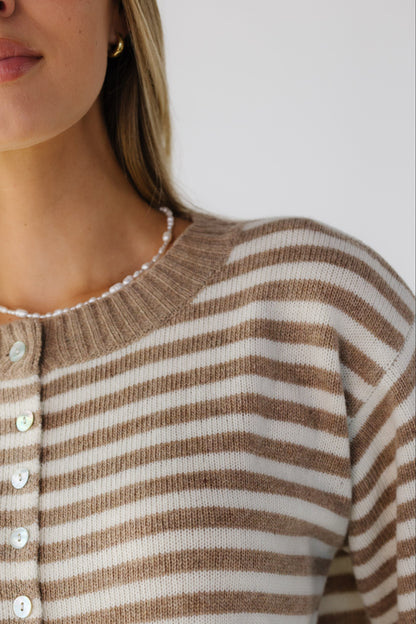 A close up view of a woman wearing a taupe & cream stripe cardigan with a wide ribbed, round neckline.