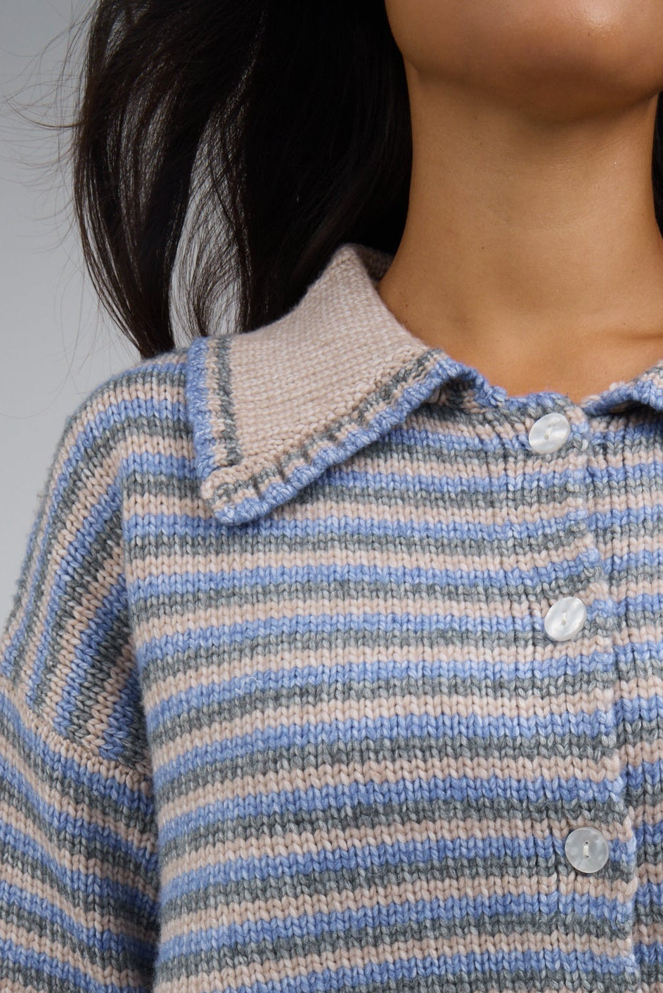 Close view of a woman wearing a blue-taupe-charcoal stripe button down cardigan with a pointed taupe collar.