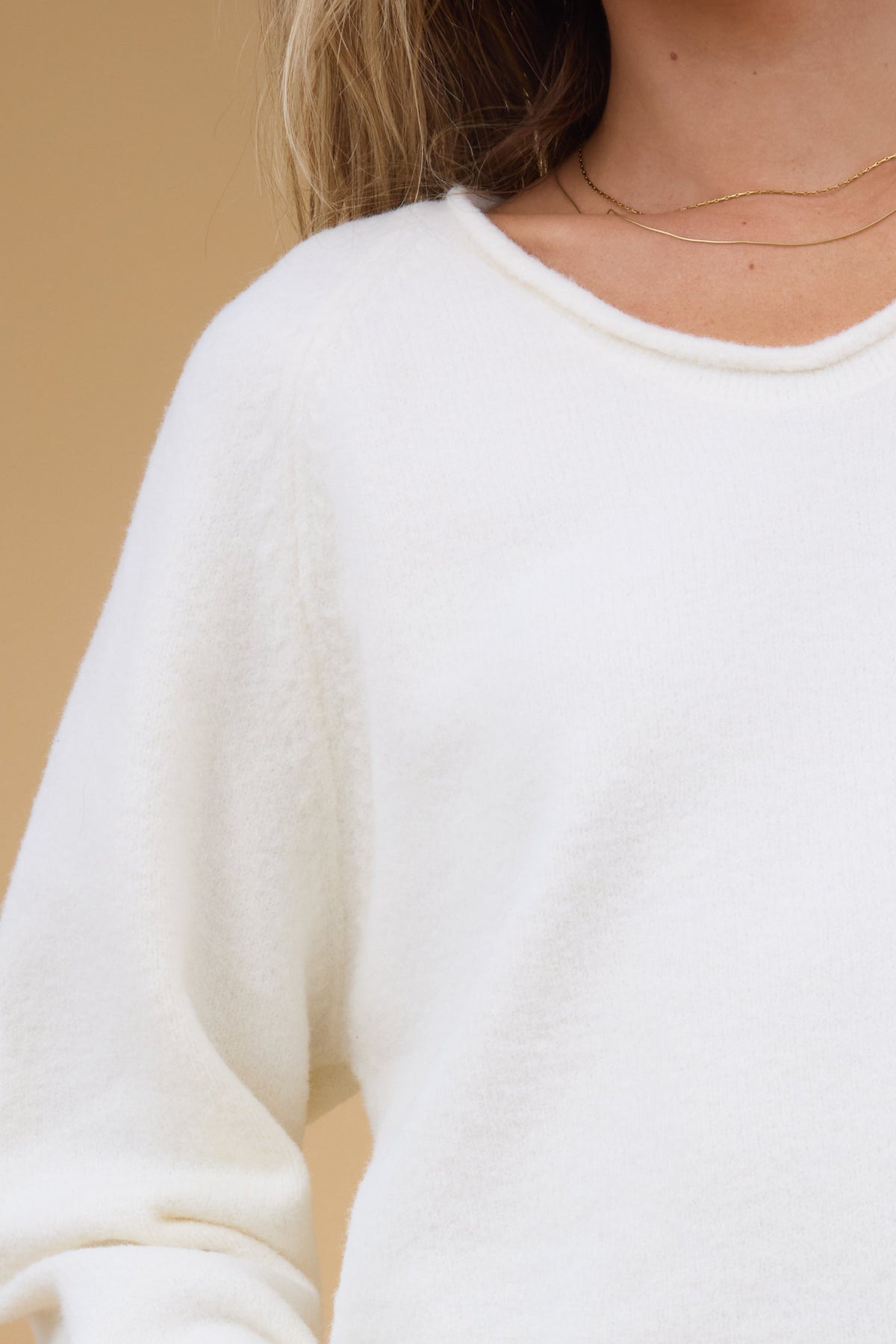 Close view of a woman wearing cream long sleeve sweater with rolled neckline.